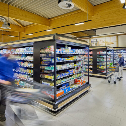 Die Kühlwarenzone mit freistehenden Mehrdeckkühlmöbeln; die Holzverkleidung der Decke zieht sich gestalterisch durch den gesamten Markt