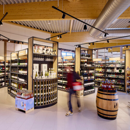 Die Weinabteilung präsentiert ihr Sortiment in Holzregalen mit Metalleinfassung; ein Holzfass dient als Aktionsfläche