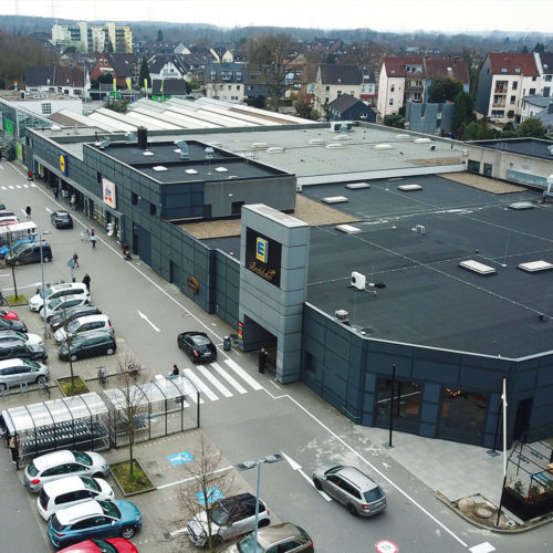 Eine dunkelgraue Streckmetallfassade bildet die Kulisse für den Edeka-Supermarkt und die anderen Ladenmarken im Fachmarktzentrum