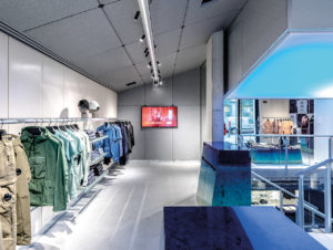 Der Mailänder Store von C.P. Company mit von der Decke abgehängter Lightbox und glänzenden Präsentationsmöbeln mit Farbverlauf