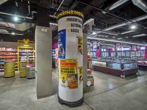 Die Litfaßsäule wurde in Berlin erfunden. Bei Edeka wirbt sie für Veranstaltungen im Markt und aktuelle AngeboteDas Center hat drei Eingänge, u. a. gelangt man von der Schloßstraße direkt über einen Fahrstuhl in den Gastro-Bereich.