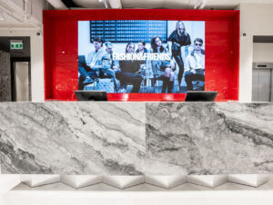 Der Kassenbereich kombiniert eine großflächige rote Nische mit marmoriertem Naturstein und beleuchteten Sitzelementen für Wartezeiten