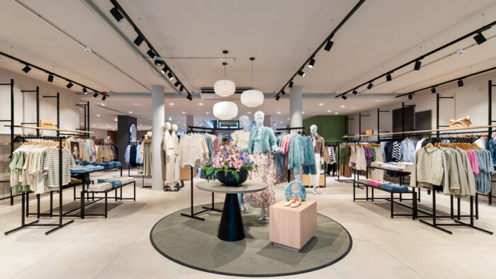 Stangensysteme, Hängelampen und ein zentraler Präsentationspunkt mit Rundteppich strukturieren den Bereich Damen Casual & Trend