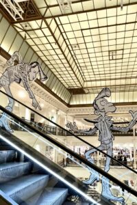 Aufsteller an Rolltreppen zeigen Comicfiguren von Didier Lembrouille: die Kultfigur des französischen Entertainers Antoine de Caunes prägt das Design des „Rock ’n‘ Drôle“-Events.