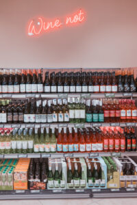 Ein Neonschriftzug über dem Weinregal fügt sich in das Gestaltungskonzept des Marktes ein
