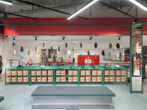 Einzelne Schuhmodelle hängen frei im Raum über dem langen grün lasierten Verkaufstisch