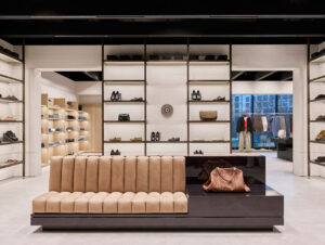 Die Schuh- und Taschenabteilung im Obergeschoss verbindet aufgeräumte Regalarchitektur mit einem skulpturalen Lounge-Sitzmöbel als gestalterischem Mittelpunkt