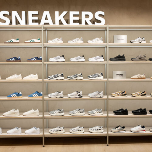 Eine raumhohe Sneaker-Wall präsentiert Modelle markenbezogen geordnet auf offenen Regalsystemen