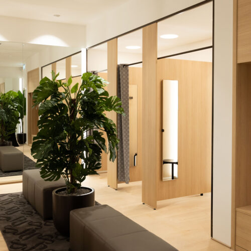 Die Umkleidekabinen sind mit hellem Holz, großformatigen Spiegeln und Pflanzendekoration gestaltet