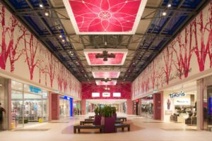 Sieger A 10 Center: Wandfluter illuminieren die grafisch gestalteten Oberflächen im Eingangsbereich. Uplights beleuchten die abgependelten Deckenfelder in den Atrien.