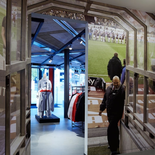 Von den Umkleiden führt ein stilisierter Stadiontunnel auf die Verkaufsfläche, in dem rechts und links großformatige Fotos den Blick aus der Spieler-Perspektive imitieren.