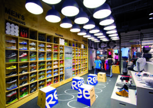 Der Reebok Fitness Hub in New York: Auffälliges Design-Merkmal ist die Dreierreihe von Pendellampen mit Metallschirm, die die Aufmerksamkeit der Kunden zur Schuhwand  lenkt