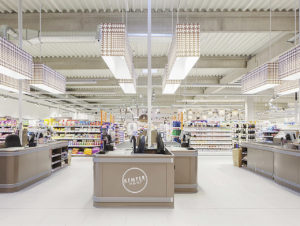 Edeka Kemper wählte für seinen neuen Markt eine ganz helle Optik in Weiß und Beige, hier der Kassenbereich mit prägnanten Lampenschirmen.