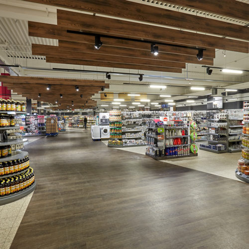 Eine Deckenkonstruktion aus Holzlamellen und der optisch von den Sortimentsbereichen abgesetzte Bodenbelag navigieren den Kunden durch den Store. (Foto: Rosendahl Fotografie)